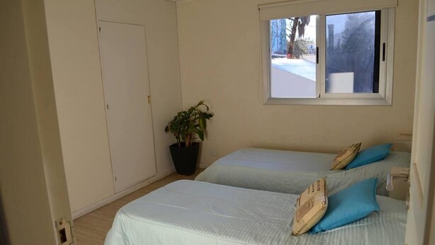 A bedroom with two beds, a window, a potted plant, and a door. - Jaque Mate Hostel (Mendoza)