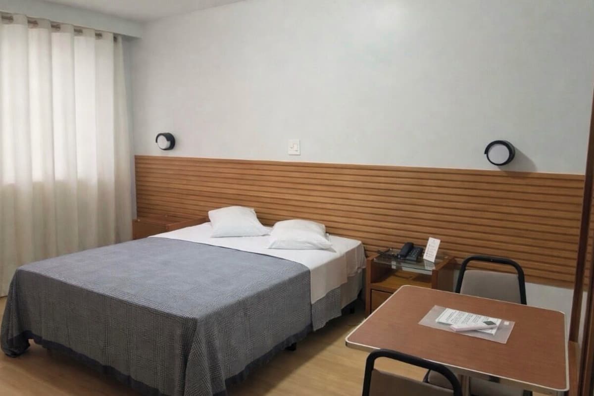 Una habitación de hotel con cama, mesa, silla y mesita de noche con teléfono.