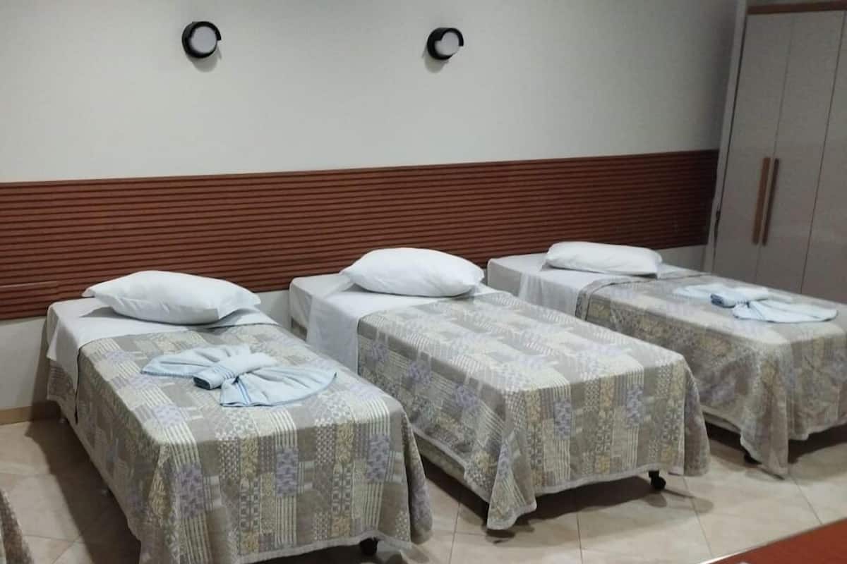 Habitación de hotel con tres camas individuales, un cabecero de madera, un armario y una mesita con un menú.