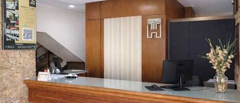 A reception desk with a wooden finish, a modern logo, a computer, and a vase with flowers.