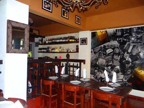 Un restaurant amb zona de bar, taules de fusta preparades per dinar i una paret amb un collage de fotografies en blanc i negre.