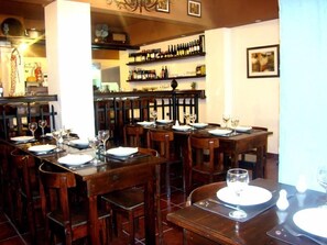 Un restaurant amb taules i caires de fusta, ampolles de vi a les prestatgeries i un rellotge a la paret.