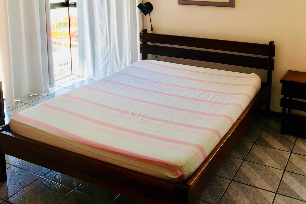 Une chambre à coucher avec un lit, un ventilateur de plafond, un tableau encadré au mur et une fenêtre avec des rideaux.