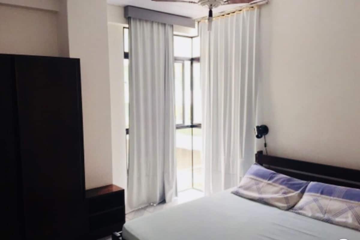 Une chambre d’hôtel avec un lit, une table de chevet, une armoire et une fenêtre avec des rideaux.