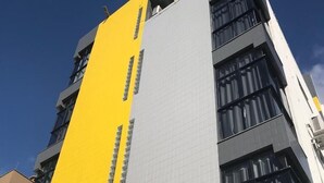 A modern building with a yellow and grey facade, large windows, and a clear sky.