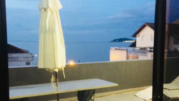 A balcony with a white table and umbrella, overlooking a body of water and buildings.