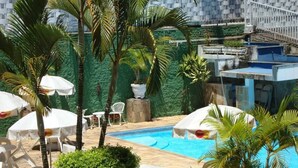 Un área de piscina con palmeras, sombrillas blancas y sillas de descanso.