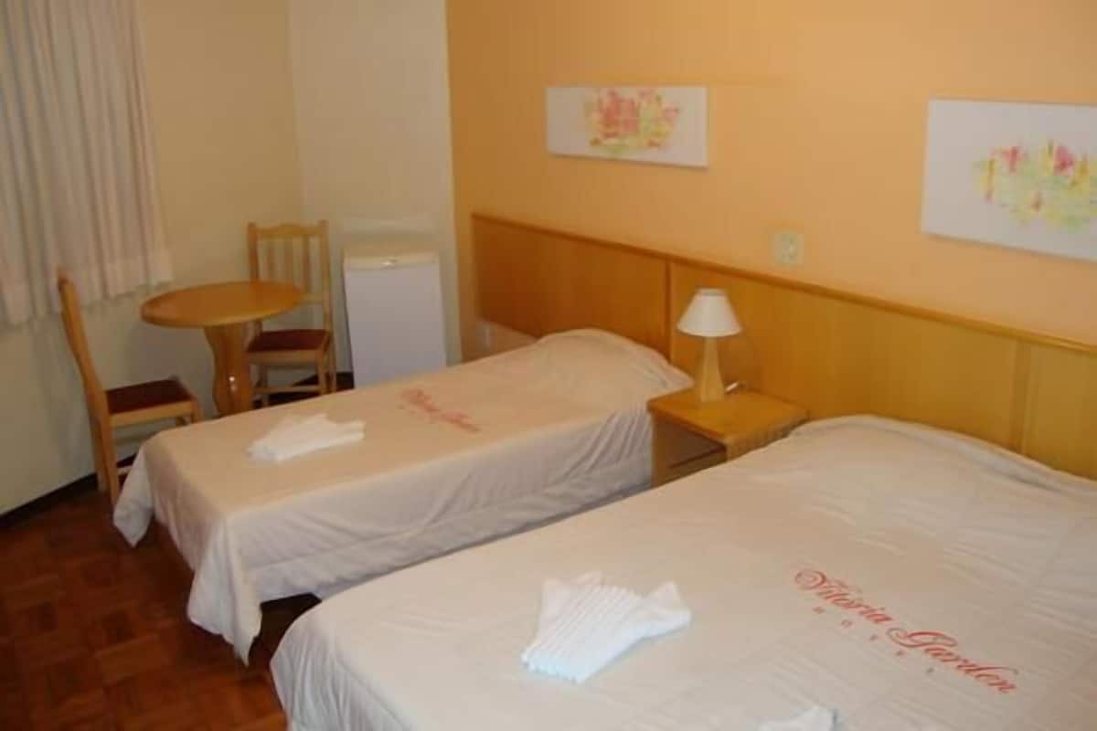 Habitación de hotel con dos camas, una mesita, una silla y una lámpara fijada a la pared.