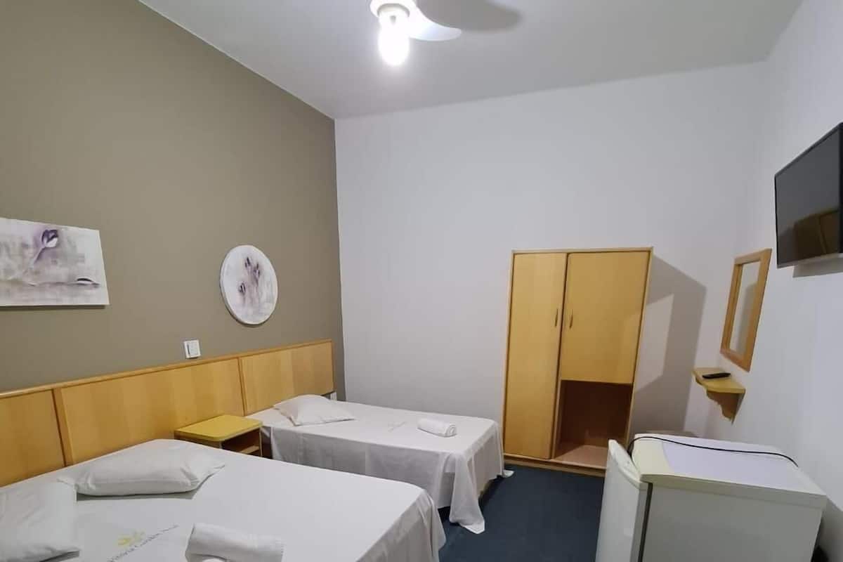 Habitación de hotel con dos camas individuales, un escritorio, un armario, ventilador de techo y televisor de pantalla plana.