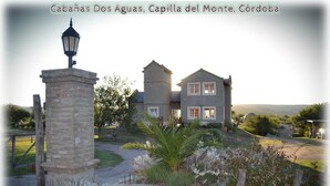 Una casa de dos pisos con entrada de piedra y un farol, rodeada de follaje y un cielo despejado.