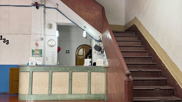 A staircase with a wooden handrail, a reception desk with a clock, and a tiled floor. - Hotel Morales Inn (Mazatlán)