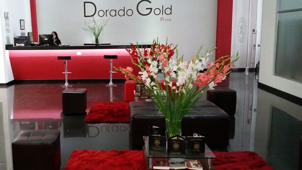 A reception area with a red and white color scheme, a reception desk, a bar area, and a seating arrangement with red cushions and a vase of flowers. - Hotel Dorado Gold Prime (Bogota)