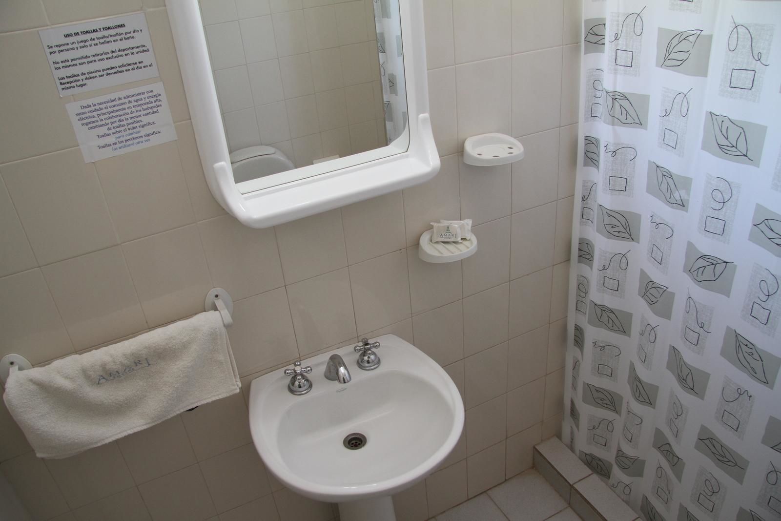 A bathroom with a sink, mirror, and towel rack. There is a shower curtain with a leaf pattern.