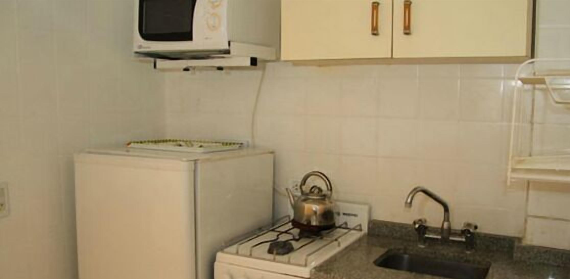 A compact kitchen with a refrigerator, a kettle, a sink, and a microwave.