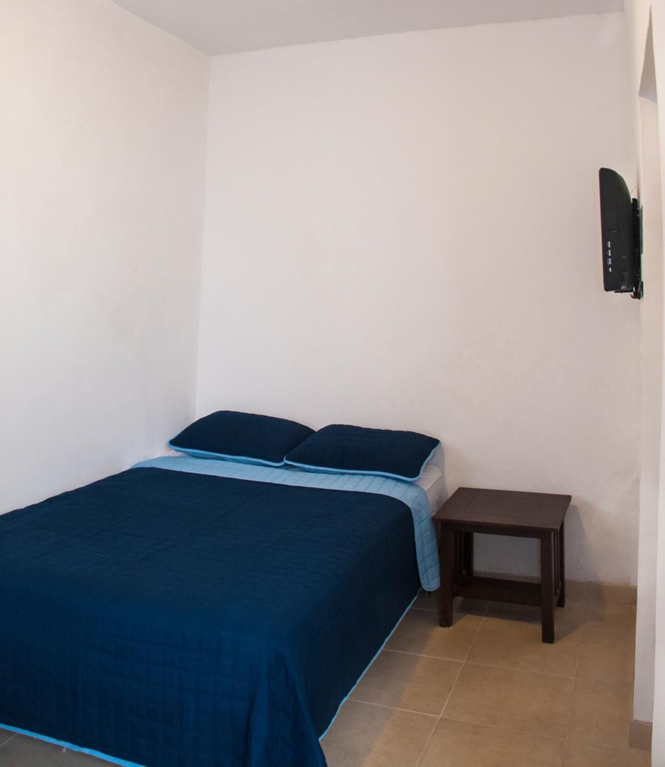 Una habitación pequeña y sencilla con una cama, una mesita de noche y un televisor en la pared.