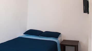 Una habitación pequeña y sencilla con una cama, una mesita de noche y un televisor en la pared.