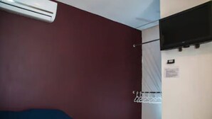 A room with a red wall, a mounted TV, and a white door. - Hotel Bugambilias (Cajeme)