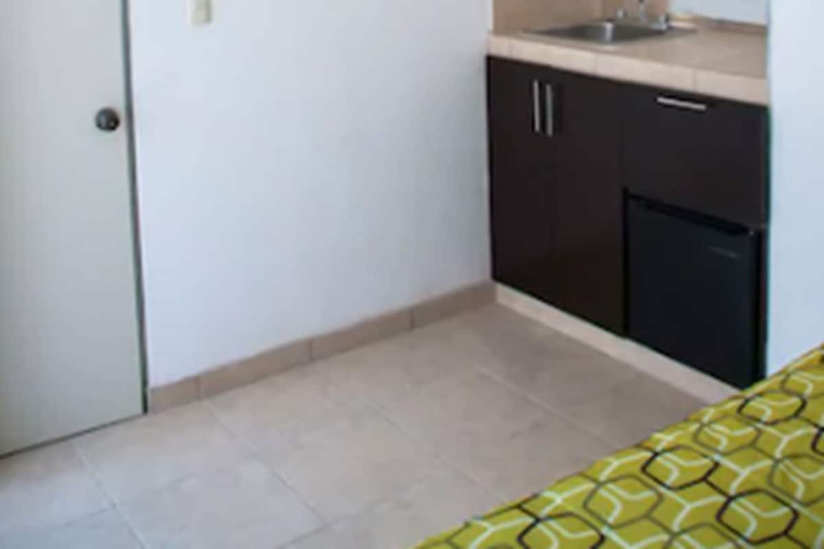 A small kitchenette with a sink, a stove, and an air conditioner mounted on the wall.