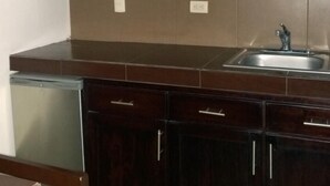 A kitchen with dark wooden cabinets, a stainless steel sink, and a built-in window above the countertop. - Hotel Bugambilias (Cajeme)