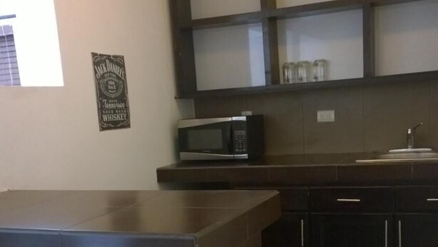 A kitchen with a dark wooden island, a microwave, and cabinets. There is a chair with a white cushion in front of the island. - Hotel Bugambilias (Cajeme)