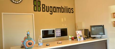 Een receptiebalie met een klok, een computer monitor en een bordje met de tekst 'Bugambilias'.