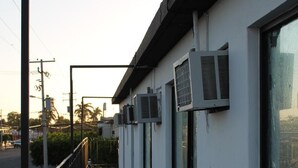 A building with multiple air conditioning units mounted on the exterior wall, a concrete sidewalk, and a metal railing. - Hotel Bugambilias (Cajeme)