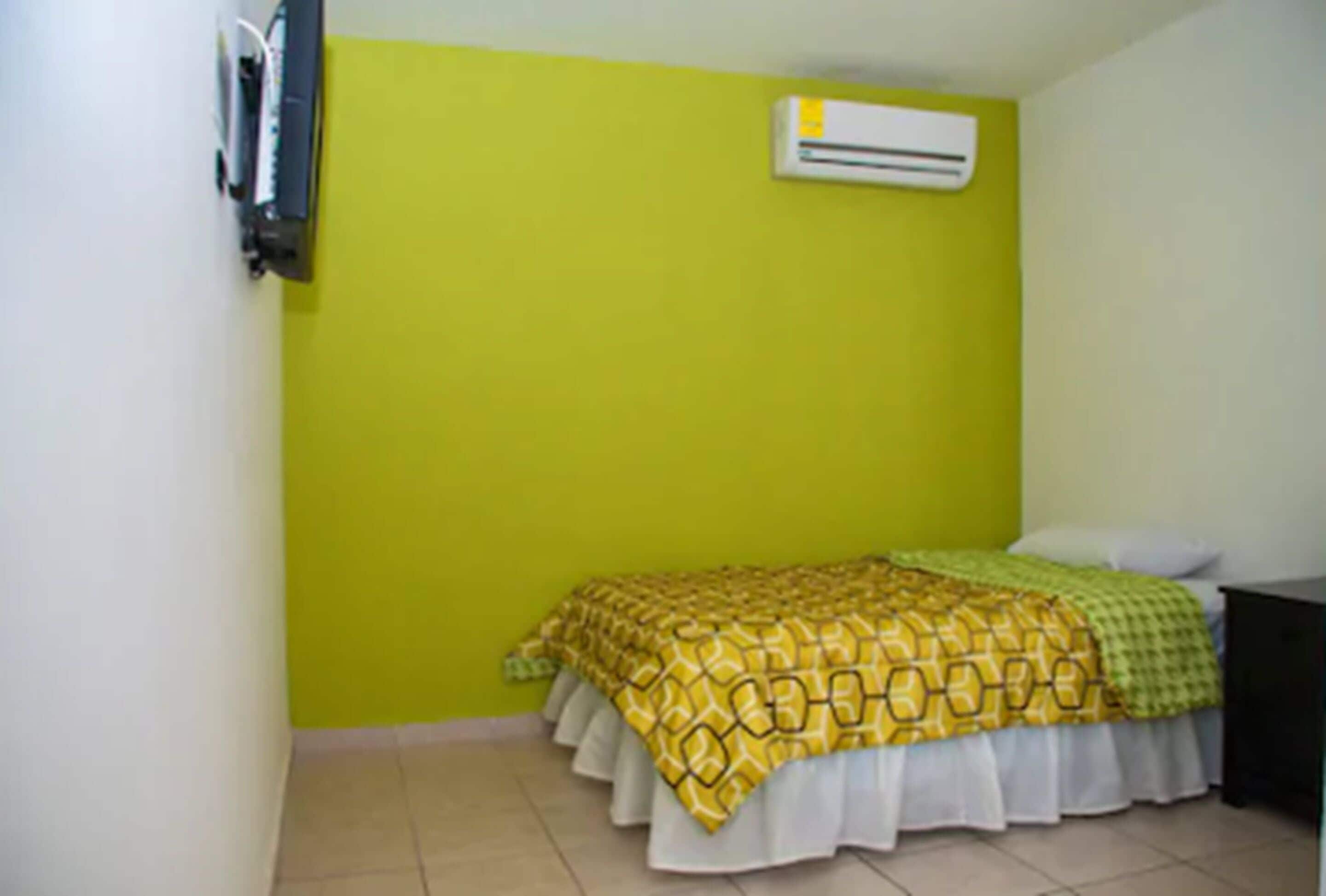 A room with a bed, a nightstand, and an air conditioning unit on the wall.