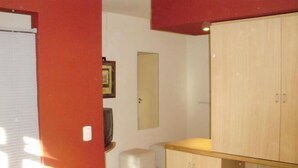 A room with a bed, a wooden wardrobe, a small stool, and a mirror on the wall. - Serú Apartments (Mendoza)