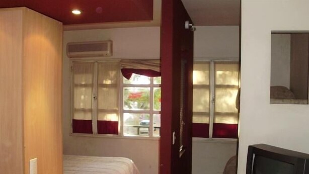 A compact room with a bed, a small desk, a television, and a window with curtains. - Serú Apartments (Mendoza)