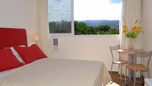 A hotel room with a large bed, a small table with chairs, and a window with a view of greenery. - Hotel Casablanca Mina Clavero (Mina Clavero)