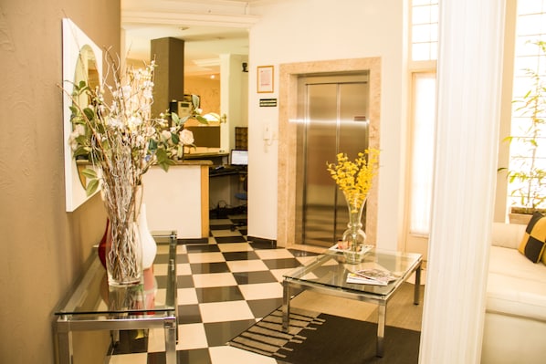 A hotel lobby with a checkered floor, a glass coffee table, a vase with flowers, a sofa, and an elevator. - Hotel Casablanca (Campinas)
