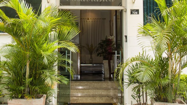 La entrada del Hotel Casablanca con un cartel sobre la puerta, plantas en macetas a ambos lados y un camino adoquinado que conduce a la entrada.