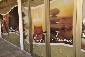 Un spa doté de portes en verre et orné de gouttelettes d’eau, avec une affiche sur laquelle on peut lire les mots « Sauna » et « Massage ».