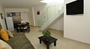 Un appartement moderne comprenant un coin repas, une cuisine, un escalier et un téléviseur à écran plat fixé au mur.