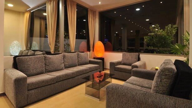 A modern living room with a grey sofa set, a glass coffee table, and a large window with curtains. - Mallak Apart Hotel (Costa Azul)