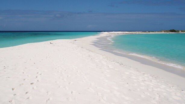 Een breed, wit zandstrand met helder turquoise water en een heldere lucht.