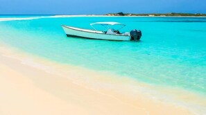 A boat on a turquoise beach with clear water and a sandy shore. - Posada Guaripete (Los Roques)