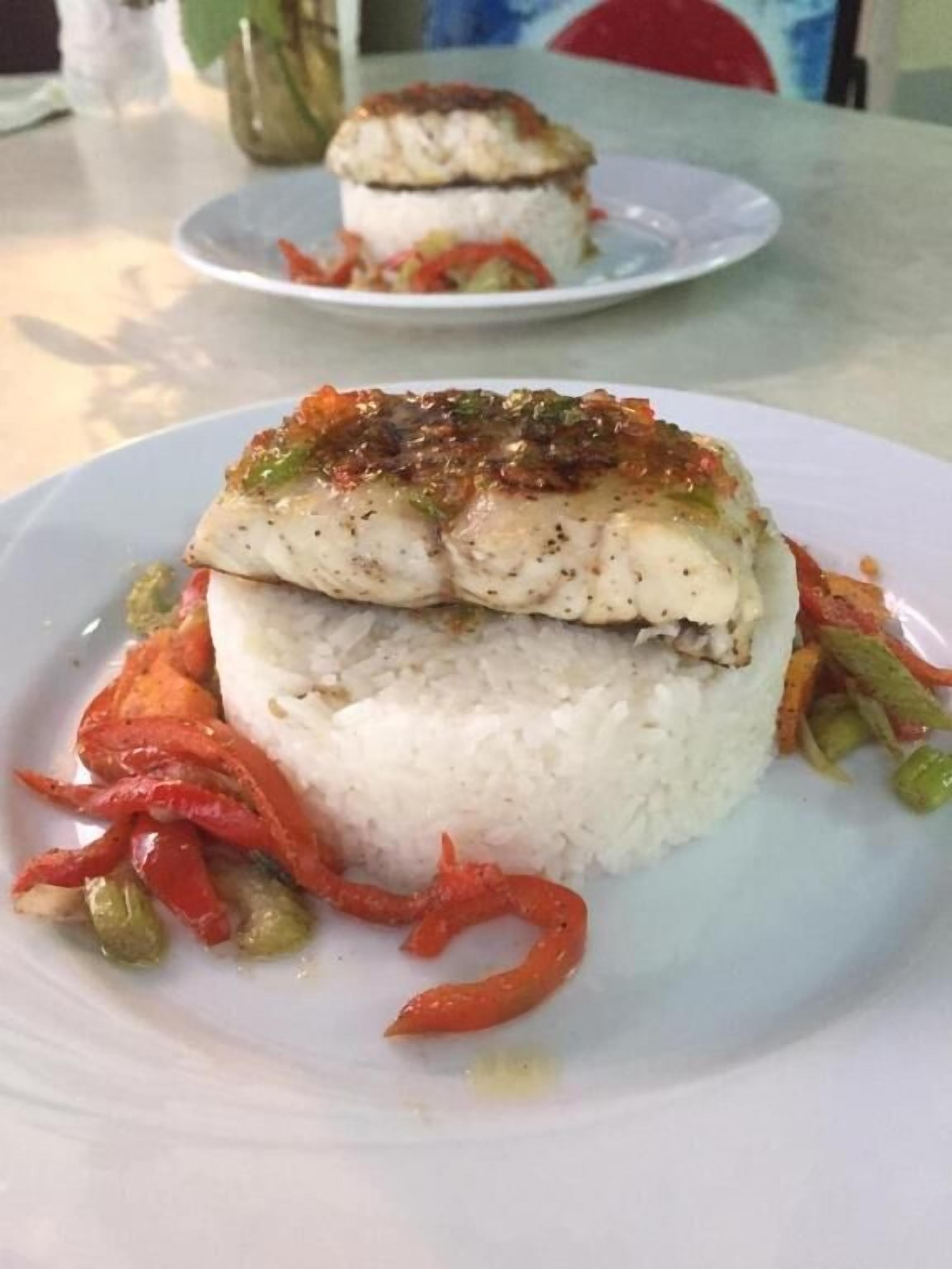 A plate with white rice, a piece of fish topped with a sauce, and red and green vegetables.