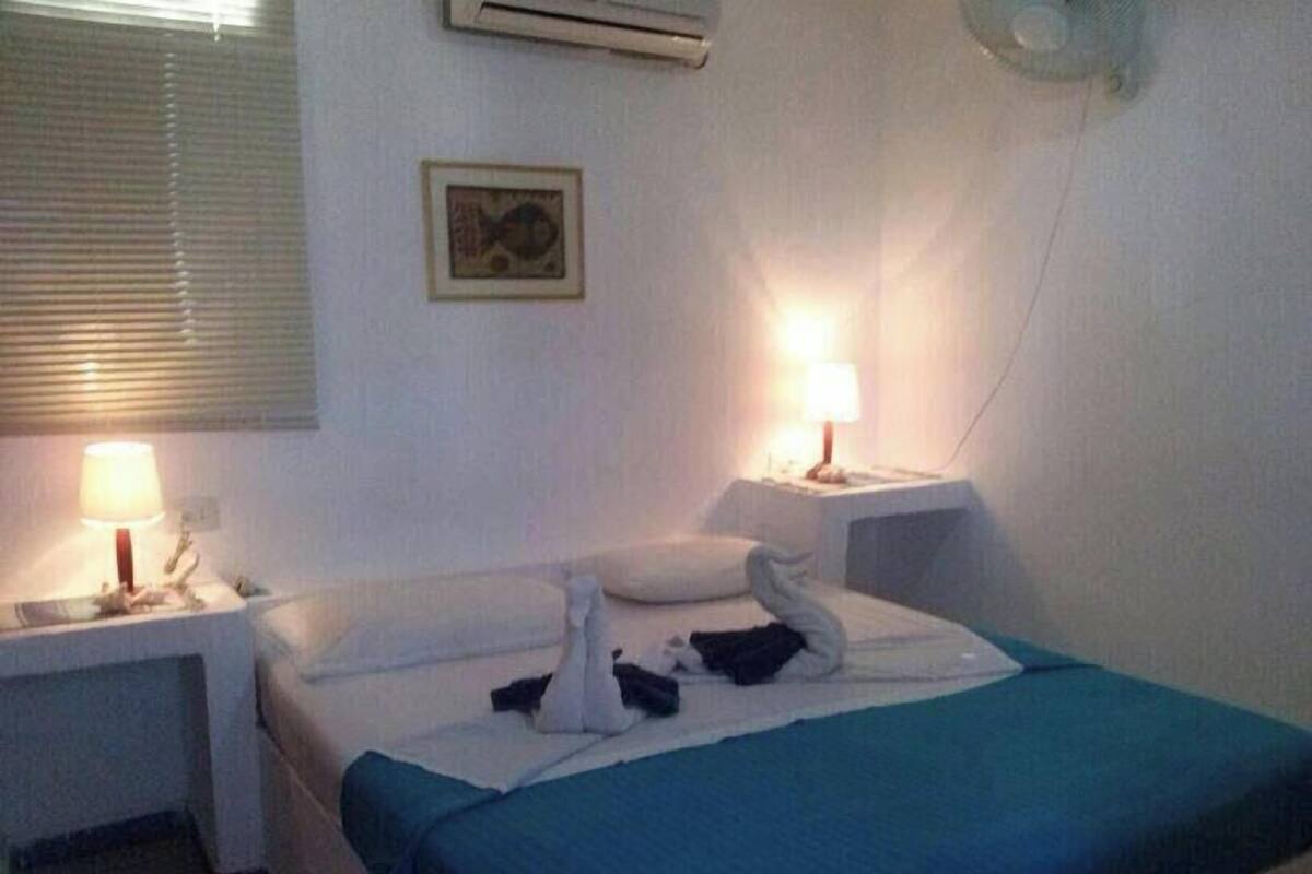 A hotel room with a bed, two bedside tables, a wall-mounted air conditioner, and a framed picture.