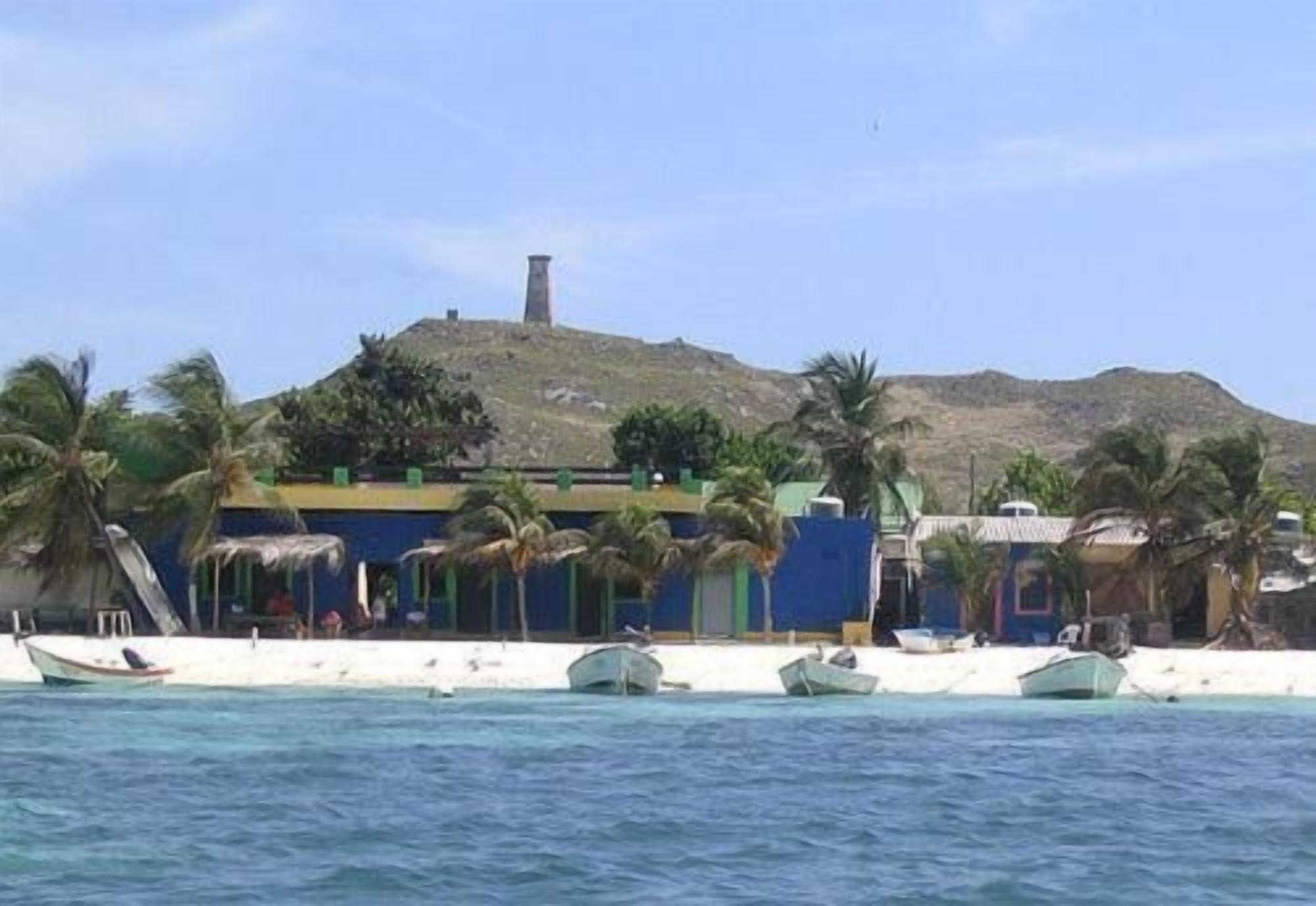 A coastal building with a prominent tower, surrounded by palm trees and boats.