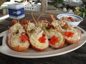 A plate of cooked lobsters with red flowers on top, placed on a wooden table. - Posada Guaripete (Los Roques)
