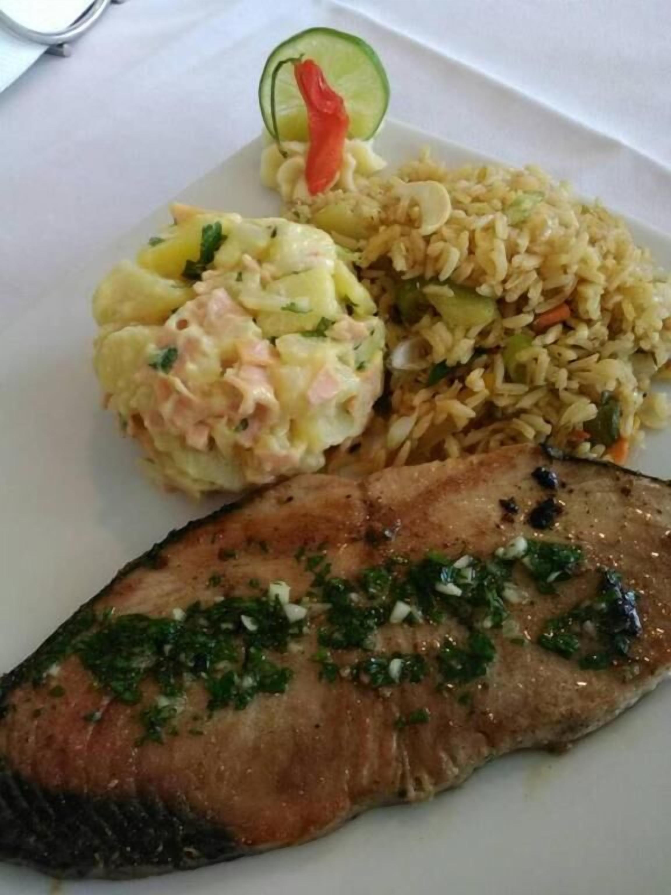 A plate with a grilled fish, rice mixed with vegetables, and a potato salad.