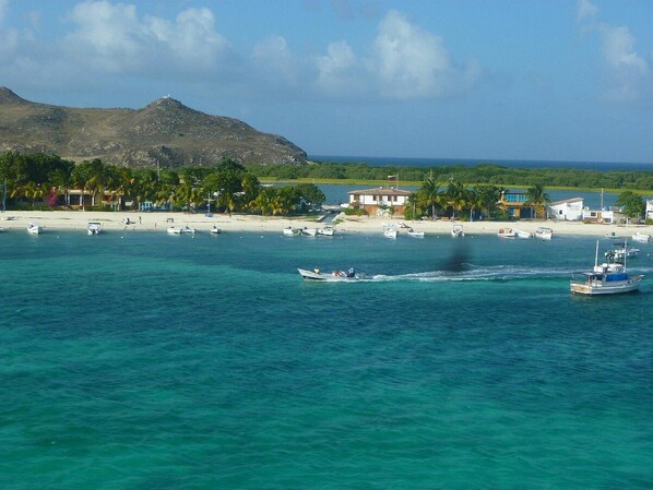 A coastal area with boats, a beach, and buildings in the background. - Posada Guaripete (Los Roques)