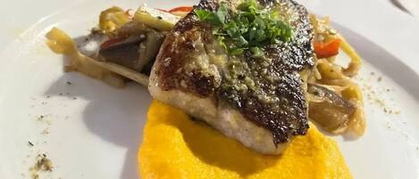 Un plato con un trozo de carne a la parrilla, verduras y un puré amarillo.