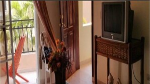 Ein Zimmer mit einer Schiebeglasdoor zum Balkon, einem HolztV-Möbel mit Fernseher und einem kleinen dekorativen Gegenstand auf dem Boden.
