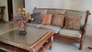 Ein Wohnzimmer mit einer Holzsofa, einem Glastisch und einer Blumenvase.