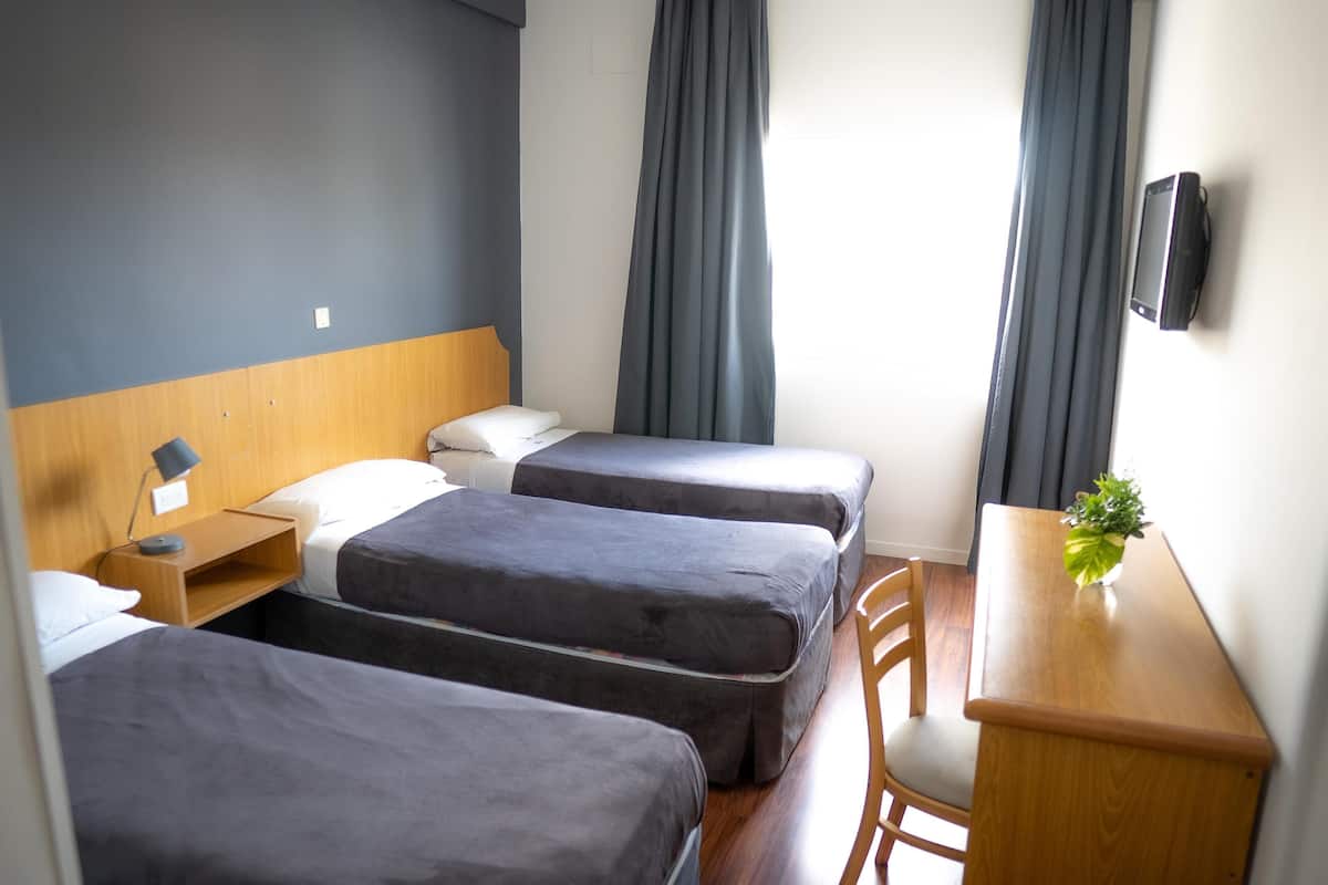 A hotel room with two beds, a desk, a chair, a TV, and a window with curtains.