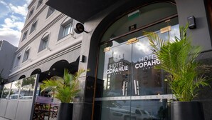 L’entrée d’un hôtel, avec une grande façade en verre, une enseigne indiquant « HÔTEL COPAHUE JUNIN » et des plantes en pot devant.