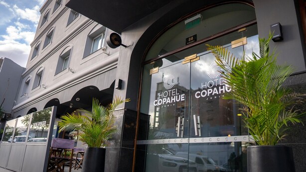 Een hotelentree met een grote glazen pui, een bord met de tekst 'HOTEL COPAHUE JUNIN' en plantenbakken voor de ingang.