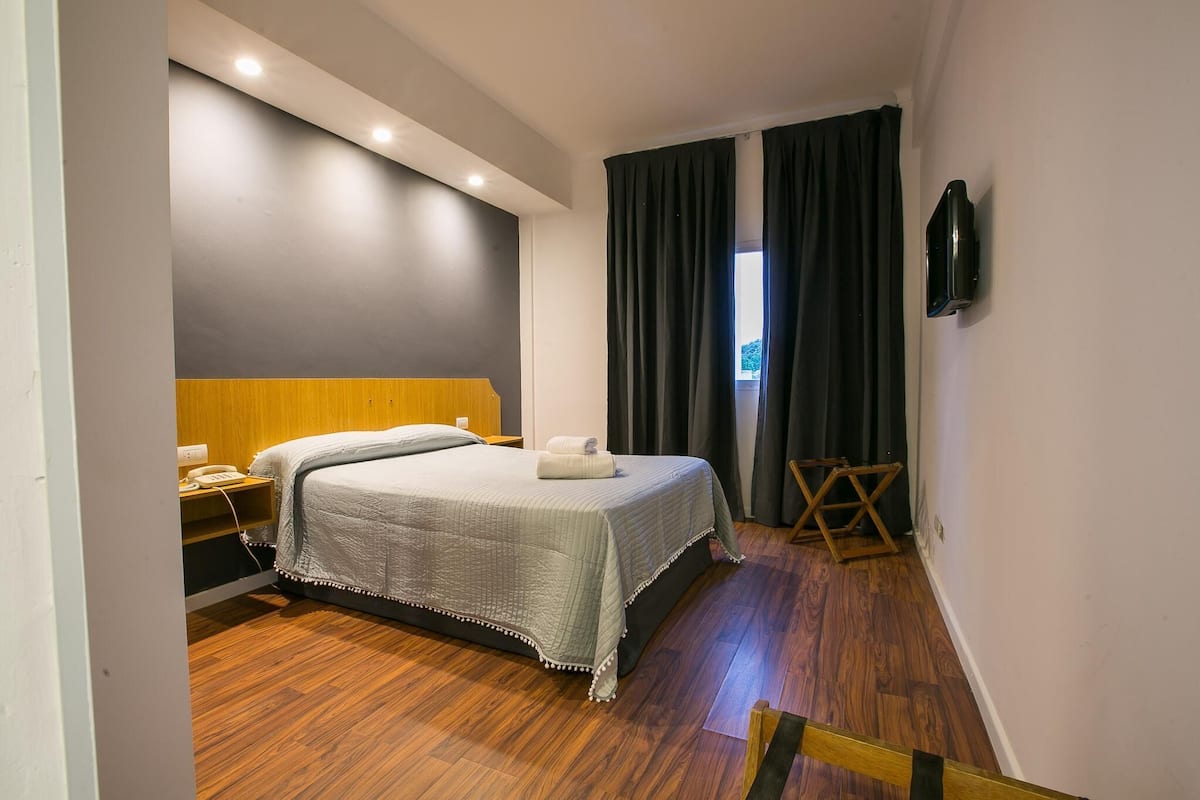 A hotel room with a bed, bedside table, and a TV mounted on the wall.